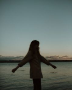 a woman standing on top of a beach next to the ocean holding her arms out