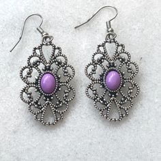 A delicate metal filigree open design drop earring centered with a small violet bead. Earring length is 1 1/14" and 3/4" wide, weighing 0.1oz each with fish-hook backs. Lightly cleaned, pre-owned and in beautiful condition. Purple Earrings With Intricate Design As Gift, Purple Earrings With Intricate Design For Gift, Ornate Purple Pierced Earrings, Purple Teardrop Metal Jewelry, Ornate Purple Jewelry With Matching Earrings, Purple Metal Drop Earrings, Purple Teardrop Metal Earrings, Purple Pierced Metal Jewelry, Purple Nickel-free Teardrop Dangle Earrings