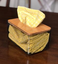 a stack of folded yellow cloths sitting on top of a wooden table next to a napkin dispenser