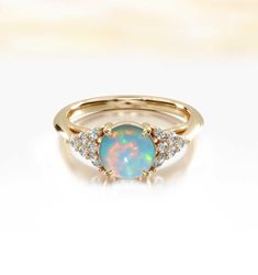 an opal and diamond ring on a white surface with the top half in yellow gold