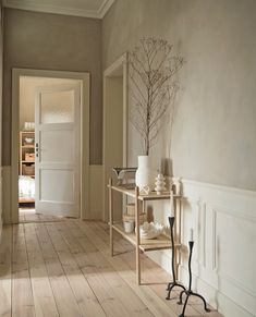 an empty hallway with wooden floors and white walls, decorated with vases and branches