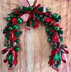 a christmas wreath hanging on the side of a wooden wall with ornaments and bows around it