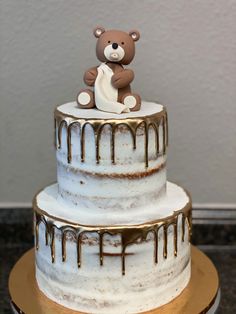 a three tiered cake with white frosting and a brown teddy bear on top