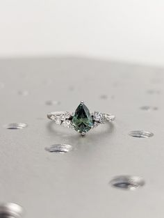 a green diamond ring sitting on top of a silver surface with drops of water around it