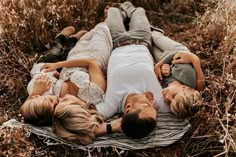 three people laying on top of each other in the middle of some tall dry grass