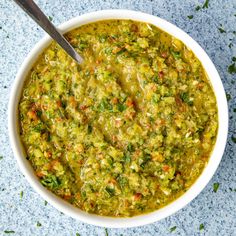 a white bowl filled with green soup on top of a blue tablecloth next to a spoon