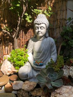 a buddha statue sitting on top of a pile of rocks next to a planter