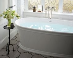 a white bath tub sitting in a bathroom next to a window with flowers on it