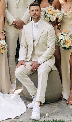 a group of people standing and sitting next to each other in formal dress clothes with bouquets