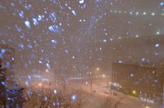 snow is falling down on the street and buildings