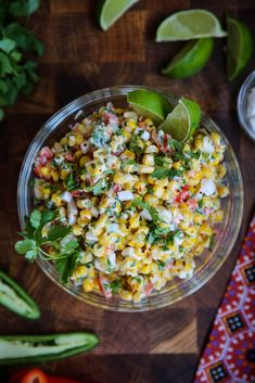 a glass bowl filled with corn and cilantro on top of a wooden table