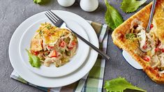 two white plates topped with food next to an egg and vegetable pot pie on top of a table