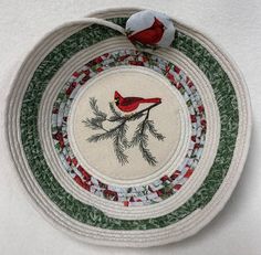 a red bird sitting on top of a green and white bowl with pine needles in the center