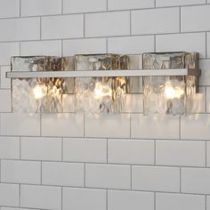 three lights are mounted on the side of a white brick wall in front of a tiled wall