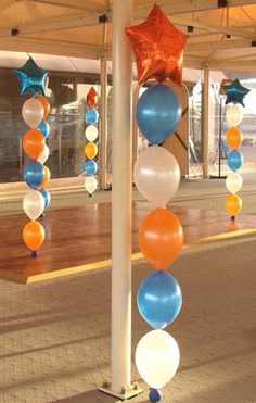 balloons and stars are hanging from poles in an open area with wood flooring on the side