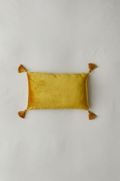 a yellow pillow with tassels on the edges is laying on a white surface