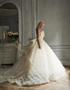 a woman in a white wedding dress standing on a wooden floor next to a mirror