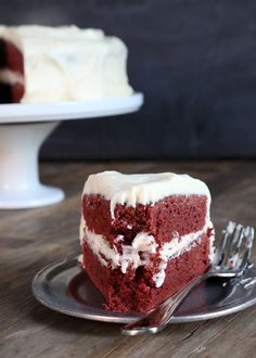 a slice of red velvet cake with white frosting on a plate next to a fork