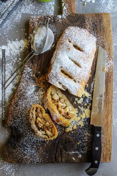 a wooden cutting board topped with pastry next to a knife and bowl filled with powdered sugar