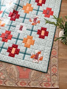 a close up of a quilt on a rug with a potted plant next to it