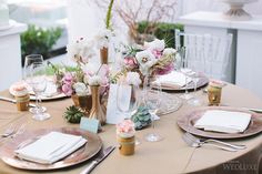 the table is set with pink and white flowers in vases, napkins, and silverware