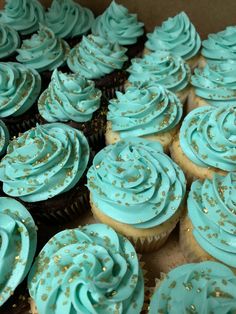 cupcakes with blue frosting and gold sprinkles in a box