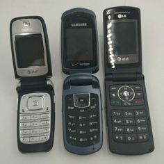 four cell phones are lined up on a white surface, one is black and the other is silver