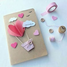 an open notebook with paper hearts attached to it next to some sewing supplies and buttons