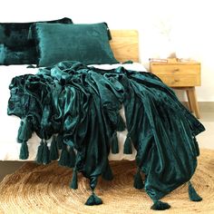 a bed covered in green velvet pillows and blankets with tassels on the headboard