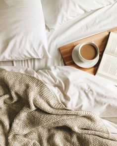 an open book and cup of coffee on top of a bed with white linens