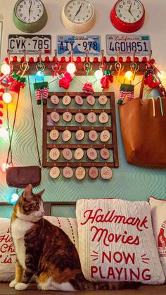 a cat sitting on top of a couch next to a wall covered in clocks and magnets