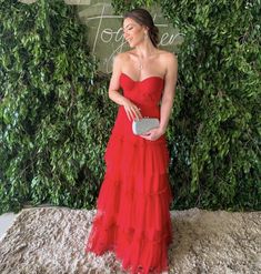 a woman standing in front of a green wall wearing a red dress and holding a purse