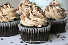 chocolate cupcakes topped with frosting and chopped nuts on a white cake plate