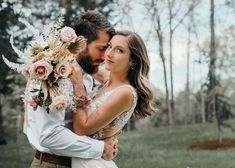 a bride and groom embracing each other in front of the woods with flowers on their wedding day