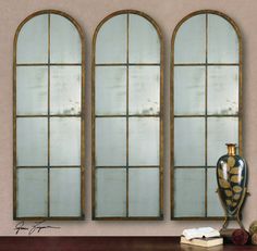 three arched windows in front of a table with a vase and books on the side