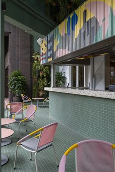 colorful chairs and tables are lined up against the wall in an outdoor cafe with potted plants