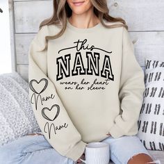 a woman sitting on a bed wearing a sweatshirt that says the nana and is holding a coffee mug