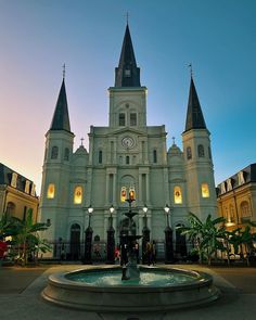 a large white building with two towers and a clock on it's face in front of a fountain