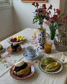 a table topped with plates of food next to vases filled with flowers and fruit