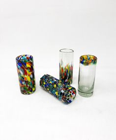 four different colored glass vases sitting next to each other on a white table top