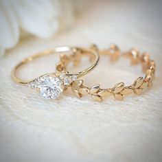 two gold rings with white stones on them sitting on a table next to a flower