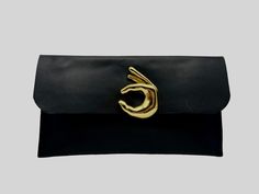 Made using the finest quality Italian leather, this clutch is super stylish and unique. A definite statement piece with a focal gold emoji accent.  It is the perfect size to fit your cell phone, keys and lipgloss for a night out and measures 10 inches in length and 7 inches inches in height.  It secures with a magnetic clasp. Trendy Black Clutch For Office, Modern Black Clutch With Magnetic Closure, Black Clutch With Magnetic Closure, Black Office Clutch With Magnetic Closure, Modern Gold Clutch For Office, Statement Clutch, Gold Clutch, Clutch Black, Black Clutch