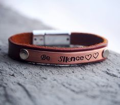 a couple of bracelets that are sitting on top of a stone surface with the words be silence written on it