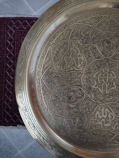 an ornate metal bowl with arabic writing on the bottom and sides, sitting on a rug