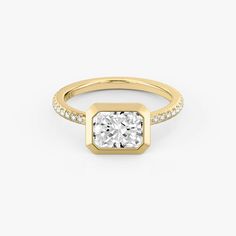 a yellow gold ring with a square cut diamond in the center and pave set shoulders