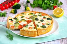 a quiche with broccoli, tomatoes and cheese on a plate next to fresh vegetables