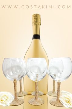 three wine glasses sitting next to a champagne bottle and two white roses on a table