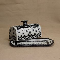 a black and white ceramic box with an ornate design on the lid, sitting on a beige background