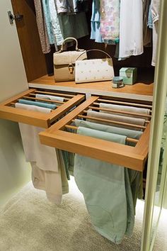 an open drawer in a closet with clothes hanging on the rack and other items inside