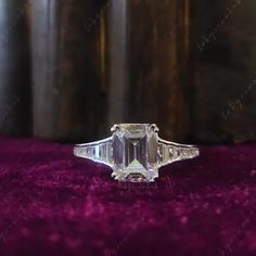 an emerald cut diamond ring sitting on purple velvet